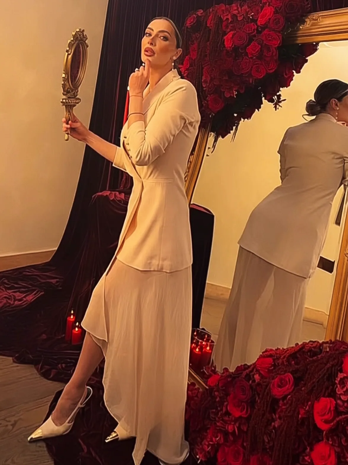 Andreea in an ivory suit, holding a gilded hand mirror beside the roses