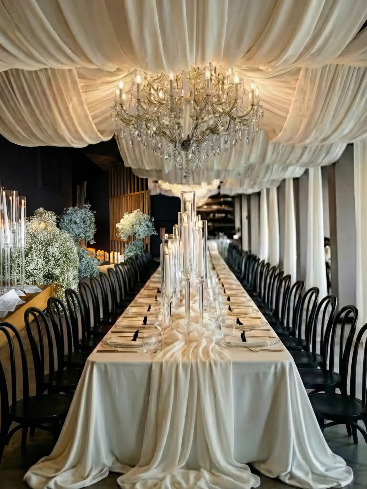 Event design by Andrinya: a long candle-lit table under draped ceilings and crystal chandeliers
